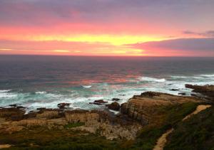 einen Sonnenuntergang über dem Meer mit Felsen im Wasser in der Unterkunft Farmhouse On The Rocks in Stilbaai