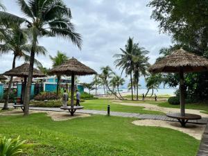 un parc avec deux bancs et parasols et la plage dans l'établissement Yussy Homestay at Cerulean Bay Forest City, à Kampong Tanjong Kupang
