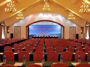 Kunming Dianchi Garden Hotel & Spa في كونمينغ: قاعة مؤتمرات مع كراسي حمراء وشاشة +246 صورة