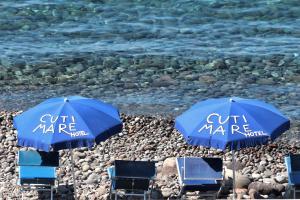 2 parasols et chaises bleus sur une plage rocheuse dans l'établissement Hotel Cutimare - Aeolian Charme, à Acquacalda