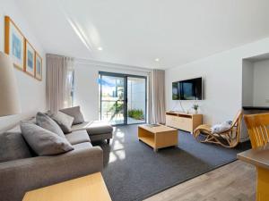 a living room with a couch and a tv at Corrigans Poolside Apartment Batehaven in Batehaven