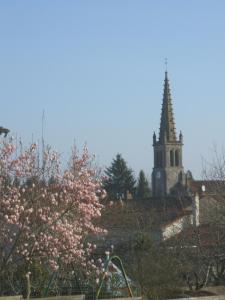 a church with a steeple and a tree with pink flowers at Chambres d'Hôtes Bienvenue in LʼAbsie
