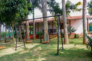 a swing set in front of a house with palm trees at Eco Serenity Pet-friendly Charming 2-BHK Villa With Lush Garden, Gazebo, Private Pool & Open Dining Close to Nandi Hills in Oddarahalli