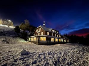 a large wooden building in the snow at night at Bílá Labuť Pec in Pec pod Sněžkou