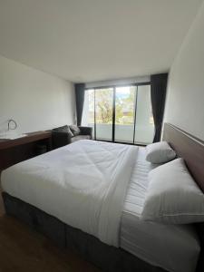 una camera da letto con un grande letto bianco con una finestra di J&P Hotel Sriracha a Ban Hua Na