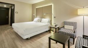 a hotel room with a white bed and a chair at NH Lleida Pirineos in Lleida
