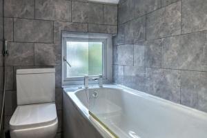 a bathroom with a tub and a toilet and a window at Stylish 2BR Cottage Pet-Friendly with Free Parking in Partington +8 photos