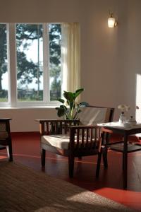 uma sala de estar com um banco, uma mesa e janelas em The Hundred House by Kisah Stays - Wayanad Colonial Estate Bungalow em Ambalavayal