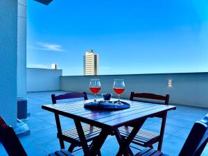 a wooden table with two glasses of wine on a balcony at Apto Penha a 300M PRAIA 8 min do BETO CARREIRO com PISICNA, sacada com CHURRASQUEIRA privativa, AR CONDICIONADO Wi Fi, PORTARIA 24h,vaga privativa de GARAGEM in Penha
