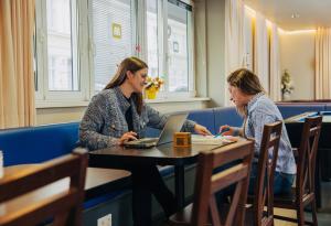 dos mujeres sentadas en una mesa con un portátil en MEININGER Hotel Wien Downtown Sissi, en Viena