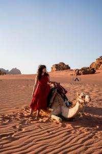 een vrouw in een rode jurk met een kameel in de woestijn bij Nadine Luxury Camp in Wadi Rum