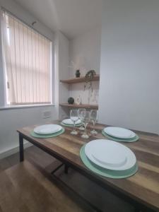 ein Holztisch mit Tellern und Weingläsern darauf in der Unterkunft Cosy 3 bed House South Shields in Jarrow