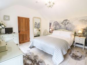 a white bedroom with a bed and a mirror at The Talkhouse Cottage in Caersws