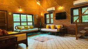 a room with a brick wall with a couch and a tv at Green Roots Farm Stay, Shahapur in Shāhāpur