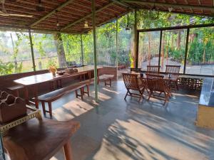 a pavilion with wooden tables and chairs and trees at Green Roots Farm Stay, Shahapur in Shāhāpur