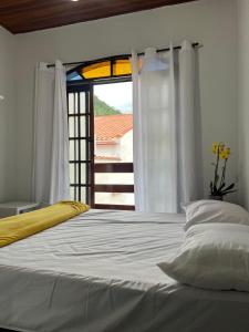 Un dormitorio con una gran cama blanca con ventana. en Hostel Bike Point Caraguatatuba, en Caraguatatuba