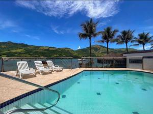 einen Pool mit zwei weißen Stühlen und Palmen in der Unterkunft Angra dos Reis - Píer 600 casa 4 in Angra dos Reis