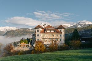 Ein großes Gebäude auf einem Hügel mit Bergen im Hintergrund in der Unterkunft Hotel Roduna in Rodeneck