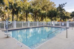 a large swimming pool with a white fence and trees at HOM Hotel Gainesville, SureStay Collection by Best Western in Gainesville