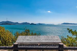 um banco de pedra sentado ao lado de uma massa de água em Kawabata Ryokan Takehara by Tabist em Takekara