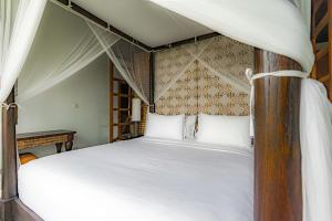 a bedroom with a canopy bed with white pillows at Uma Stana Villa in Ubud