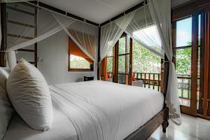 a bedroom with a bed with white sheets and windows at Uma Stana Villa in Ubud