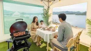 Eine Familie sitzt an einem Tisch mit Grill in der Unterkunft Chuncheon El Dorado Kid's Pension in Gapyeong