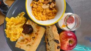 a plate of breakfast food with a bowl of scrambled eggs and an apple at Hostel del Lago, habitaciones privadas y cabañas in El Chalten +99 photos