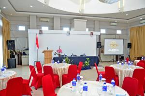 Alodia Powered by Archipelago في Tanjungkarang: قاعة اجتماعات مع طاولات وكراسي حمراء وشاشة