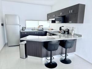 a kitchen with a counter with two bar stools and a refrigerator at Casa Honeybun in Mérida