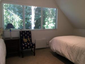 a bedroom with a bed and a chair and a window at Sunny Glen Cottage in Waikanae