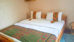 1 Schlafzimmer mit 2 Betten mit weißer Bettwäsche und bunten Kissen in der Unterkunft New Casa Gorilla Lodge and Campsite in Kisoro