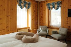 Un dormitorio con dos sillas y una cama con una almohada con forma de perro. en Hotel Bernina, en Pontresina