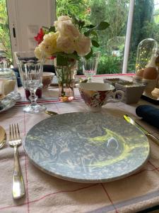 einen Tisch mit einem Teller und eine Vase mit Blumen in der Unterkunft L Orée du Bois in Agnetz