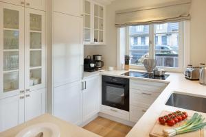 una cucina con armadi bianchi e pomodori su un tagliere di Strandhafer a List