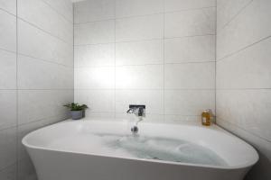 a white bath tub in a white tiled bathroom at 3 The Manor - Opposite a golf course - Pet friendly - Wi-Fi in Uny Lelant +35 photos