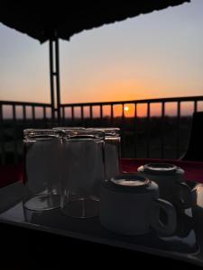 Een dienblad met glazen en mokken op een balkon met de zonsondergang op de achtergrond. bij Silver Green Resort in Gumgaon