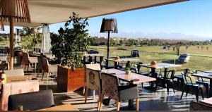 a restaurant with tables and chairs and a view of a golf course at l'écrin de prestigia agate studio in Marrakesh