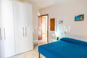 a white bedroom with a blue bed and a corridor at Castello 9 in Isola del Giglio