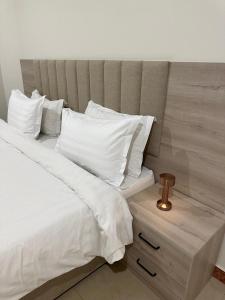 شقق رحابة المكان للشقق المفروشه في الخرج: سرير بملاءات ومخدات بيضاء بجانب موقف ليلي