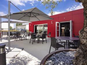 Un edificio rojo con mesas, sillas y un paraguas en ibis Dijon Sud, en Perrigny-lès-Dijon