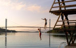 Zwei Personen springen vor einer Brücke ins Wasser. in der Unterkunft Amazing Home In Myggenäs With Sauna in Höviksnäs + 11 Fotos
