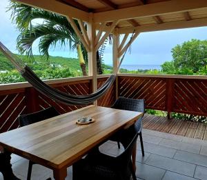 a hammock on a porch with a wooden table and chairs at Caraïbes Cottages Le Jasmin vue mer a 500m de la plage in Deshaies