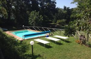 a swimming pool with two white benches in the grass at Agriturismo Casa Olinto in Sarteano
