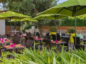 an outdoor patio with tables and chairs with green umbrellas at Novotel Paris Orly Rungis Aéroport in Rungis