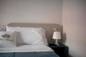 a bed with white pillows and a table with a lamp at Rosa Rooms Pompei in Pompei