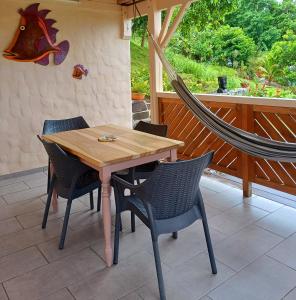 a wooden table and chairs on a patio with a hammock at Caraïbes Cottages Le Jasmin vue mer a 500m de la plage in Deshaies