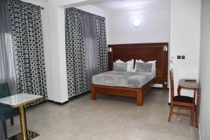 ein Schlafzimmer mit einem Bett, einem Tisch und einem Stuhl in der Unterkunft Jad Hotel Dschang in Dschang