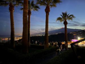 um grupo de pessoas em pé sob palmeiras à noite em Paradise By The Sea em Taormina