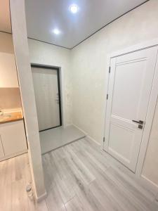 een lege kamer met een witte deur en houten vloeren bij Кокшебель Жк in Astana